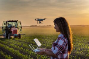 Młodzież na wsi, młoda kobieta sterująca dronem nad polem